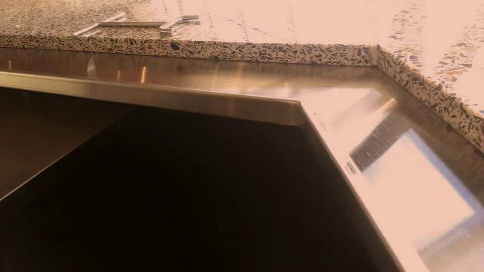 Close up of a custom stainless steel countertop edge fitted against terrazzo, stainless fabrication in Norristown PA