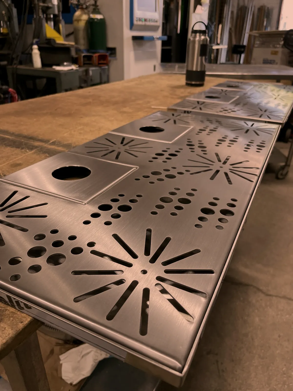 Laser cut perforated stainless sheet metal panels on the bench with the fiber laser behind, O'Donnell Metal Fab Norristown PA